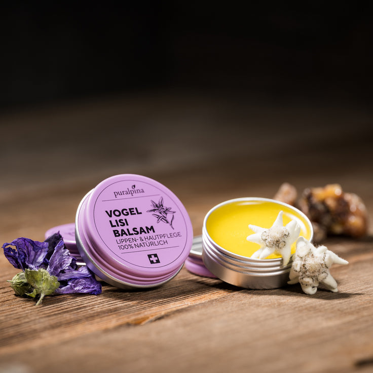 Opened and closed tin of Puralpina Vogellisi balsam with violet flowers and edelweiss on a wooden table